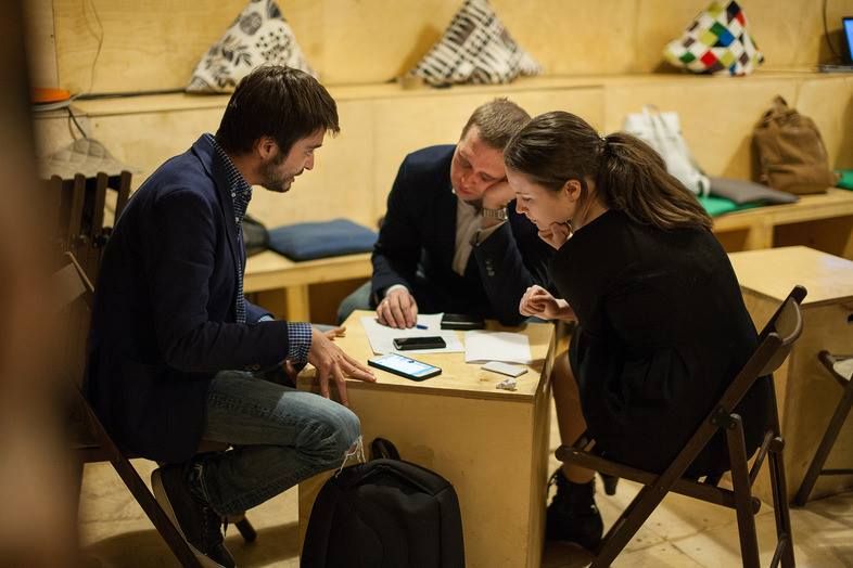 Three people bent over notes at a small table